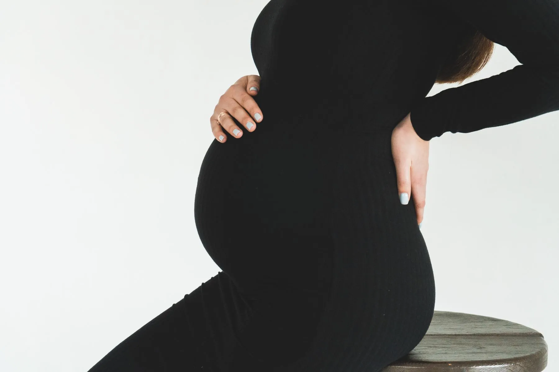 Schwangere stützt im Sitzen Bauch und unteren Rücken – Symbolbild für typische Schwangerschaftsbeschwerden